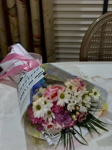 Nostaljik gazete baskılı ve şeffaf ambalaj kağıtlarına sarılarak pembe kurdeleyle bağlanmış pembe laleler mor krizantemler ve taze beyaz papatya çiçekleri.
