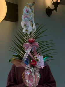 Parlak holografik ambalaj kağıdı ve pembe kurdele ile tasarlanmış geniş yeşil palmiye yaprakları üzerindeki taze mavi orkide çiçekleri.