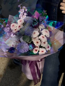 Holografik ve pembe ambalaj kağıtlarına sarılmış mor kurdeleli mor lale ve eflatun krizantem çiçeklerinden oluşan buket.