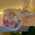 Beyaz renkli kırışık dokulu ambalaj kağıdına sarılmış ince pembe kurdeleli taze açık pembe gül ve beyaz krizantem çiçekleri.