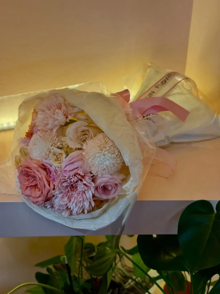 Beyaz renkli kırışık dokulu ambalaj kağıdına sarılmış ince pembe kurdeleli taze açık pembe gül ve beyaz krizantem çiçekleri.