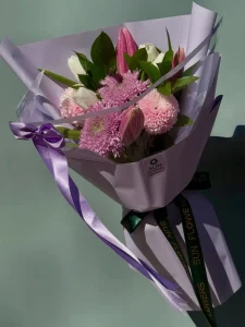 Mat lila rengi ambalaj kağıdına sarılı pembe lilyum, krizantem, beyaz laleler ve mor kurdele.