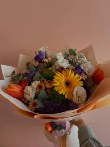 Şeftali tonlarında mat ambalaj kağıdına sarılı turuncu laleler, beyaz güller ve sarı gerbera.