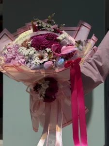Canlı fuşya ambalaj içerisinde mor kasımpatı ve taze pembe lalelerden oluşan buket