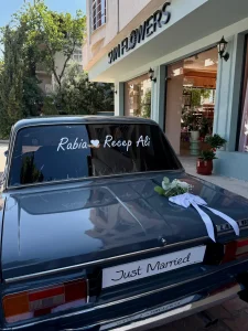 Klasik mavi araba kaputunda beyaz gül okaliptus aranjmanı ve siyah kurdeleli vintage gelin arabası süslemesi