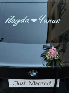 Siyah lüks araç kaputunda pembe lilyum aranjmanı ve kapı kollarında siyah beyaz kurdeleli incili gelin arabası süslemesi