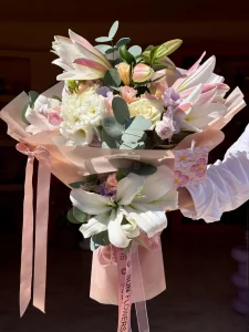 Pudra pembe ambalaj kağıdına sarılı pembe oriental lilyum beyaz gül ve lisyantus buketi
