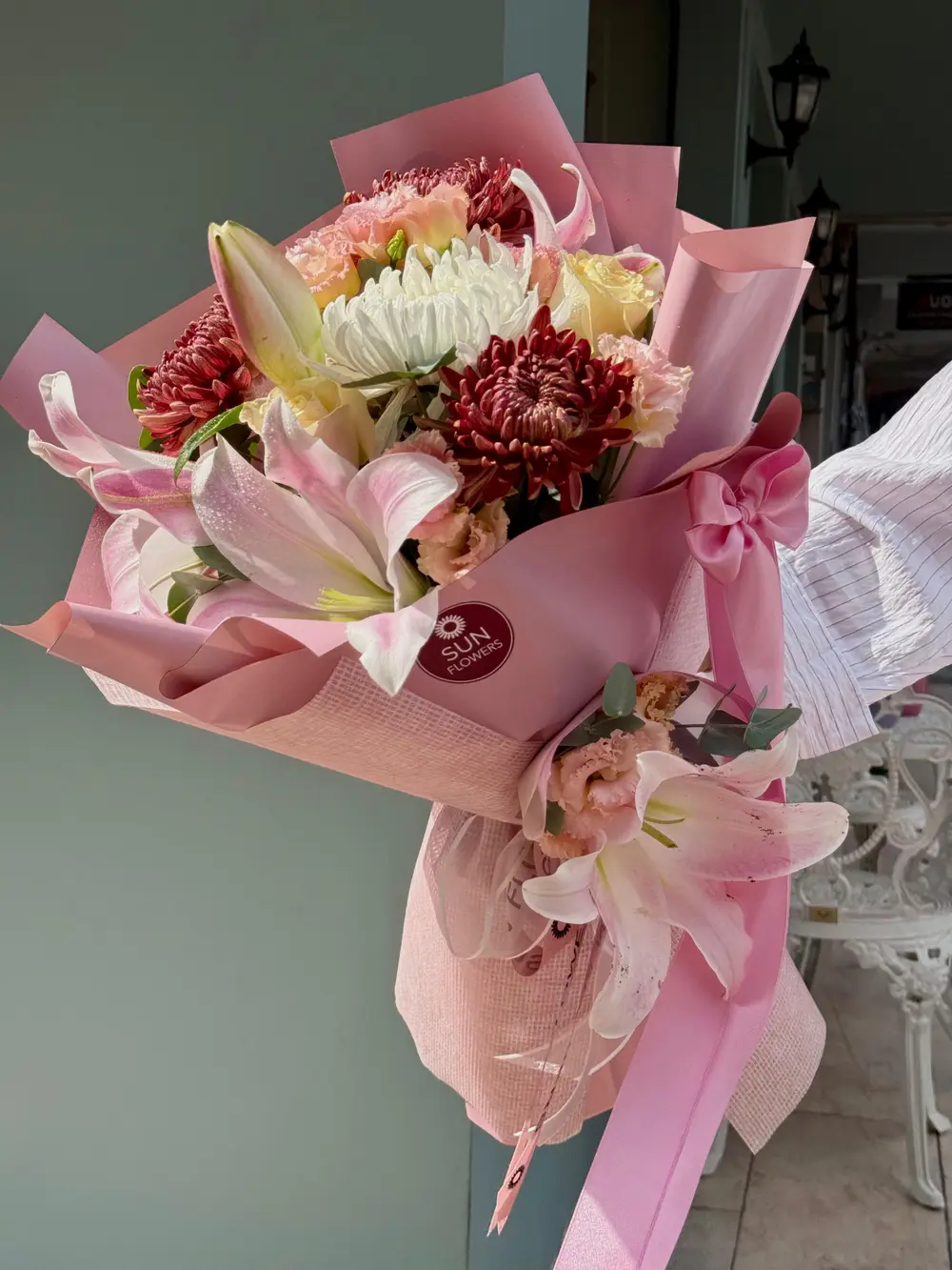 Dokulu pembe ambalaj kağıdına sarılı pembe lilyum bordo krizantem ve beyaz çiçek buketi
